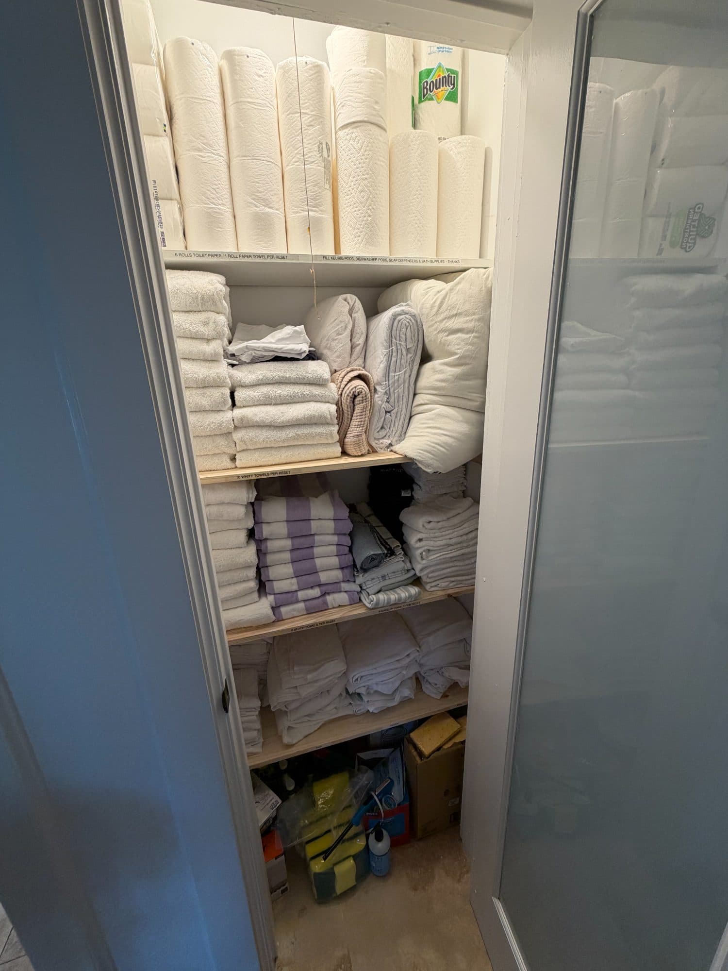 Supply closet after: built shelves with folded towels and paper goods, each shelf labeled with its par count