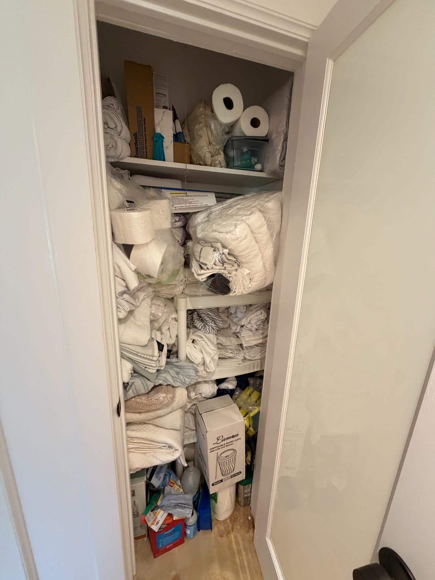Supply closet before: sagging wire shelves packed with unsorted linens, boxes and cleaning supplies