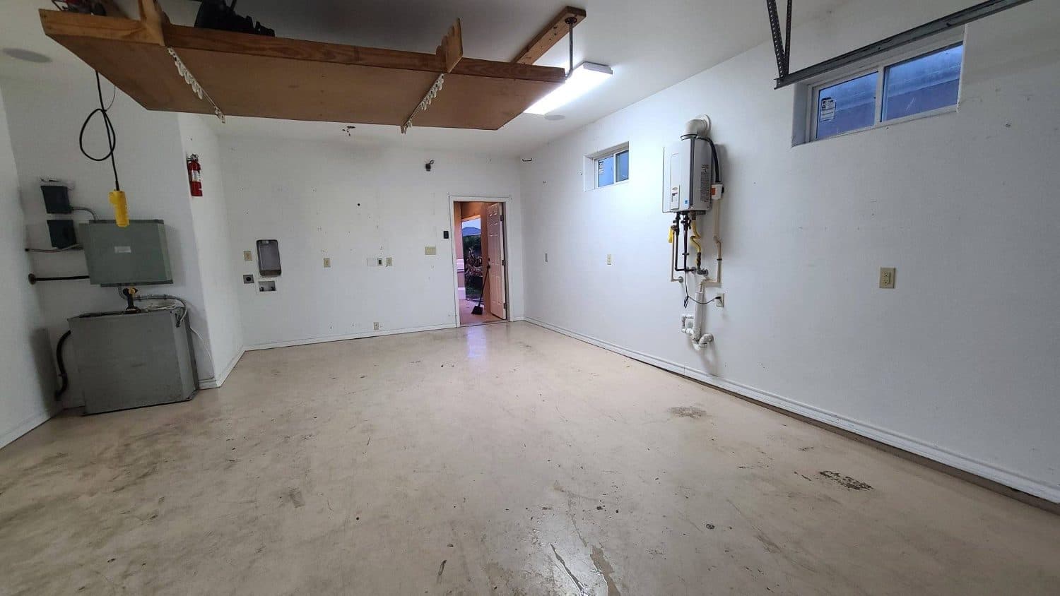 Garage before: bare white walls, stained concrete slab, exposed panels and water heater