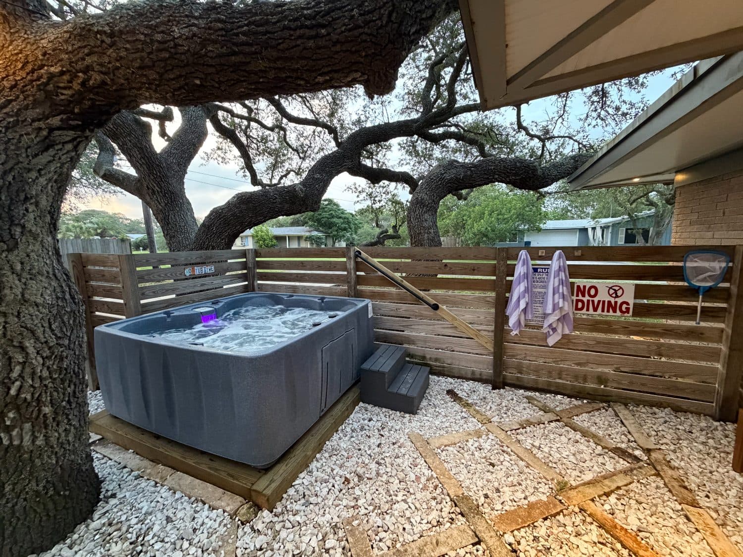 Hot tub after: installed and running under a live oak, with steps, handrail, towels and signage