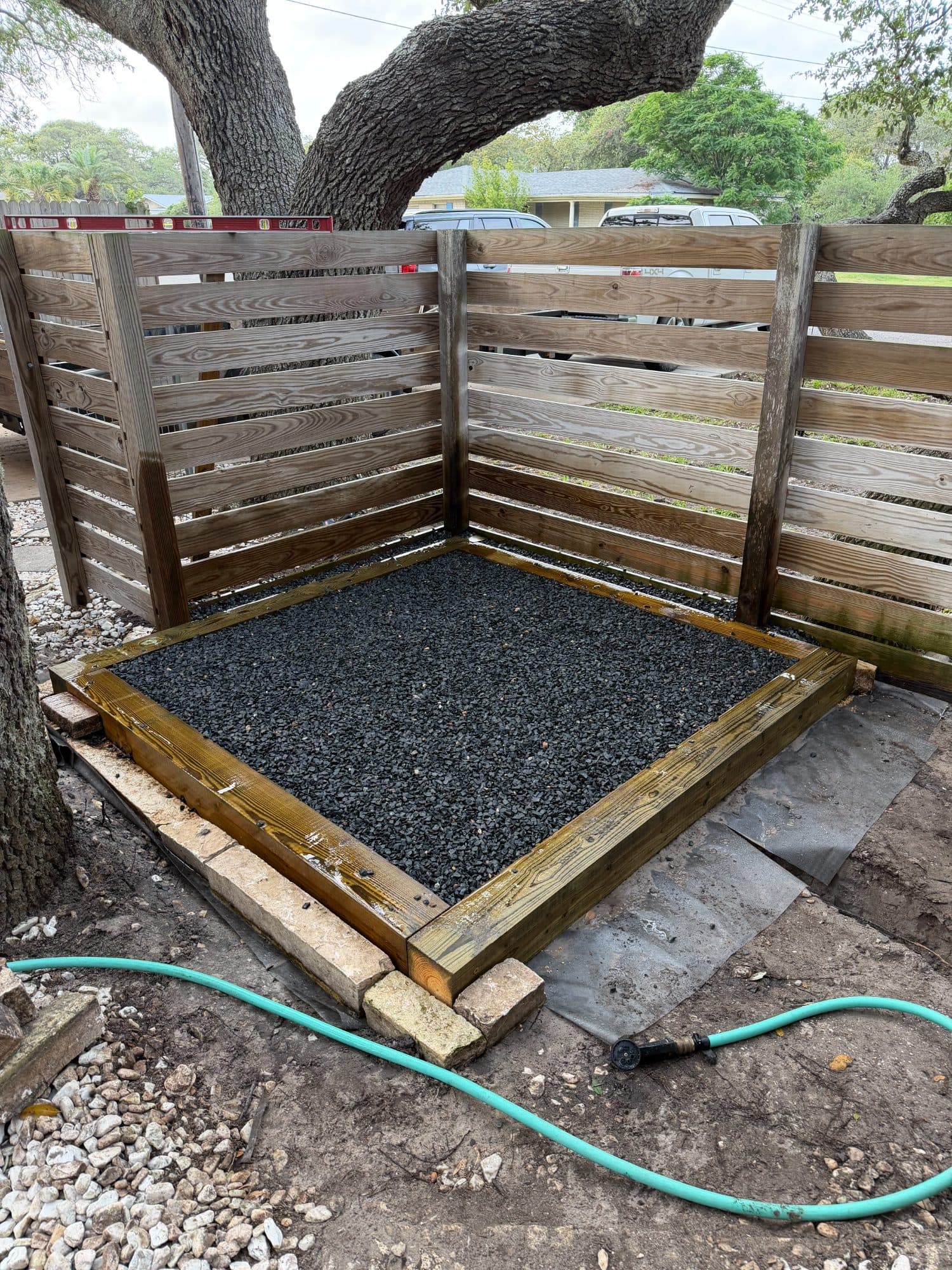 Hot tub pad in progress: leveled timber frame filled with drainage rock in the corner of a privacy fence